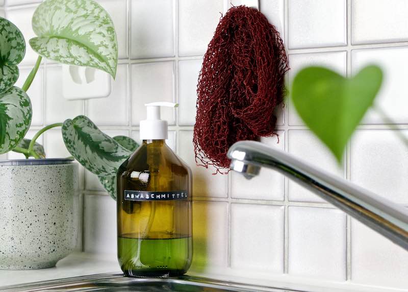 Zoom auf Fischnetz Spülschwamm Alternative in der Küche. Das Netz hängt an der Wand über einer Spüle mit Wasserhahn.